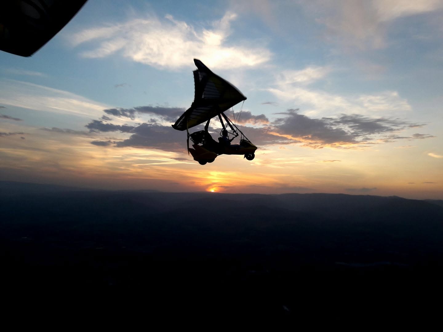 ULM pendulaire en silhouette devant un coucher de soleil sur les collines ardéchoises